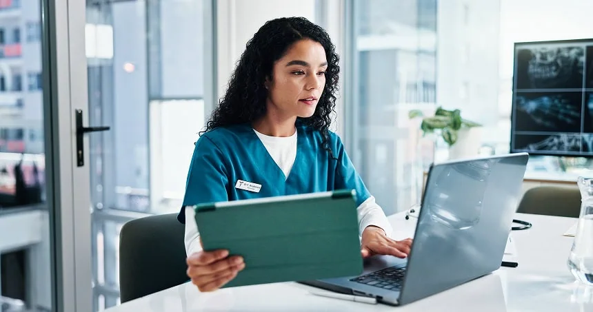 Healthcare professional using a tablet and laptop at a desk